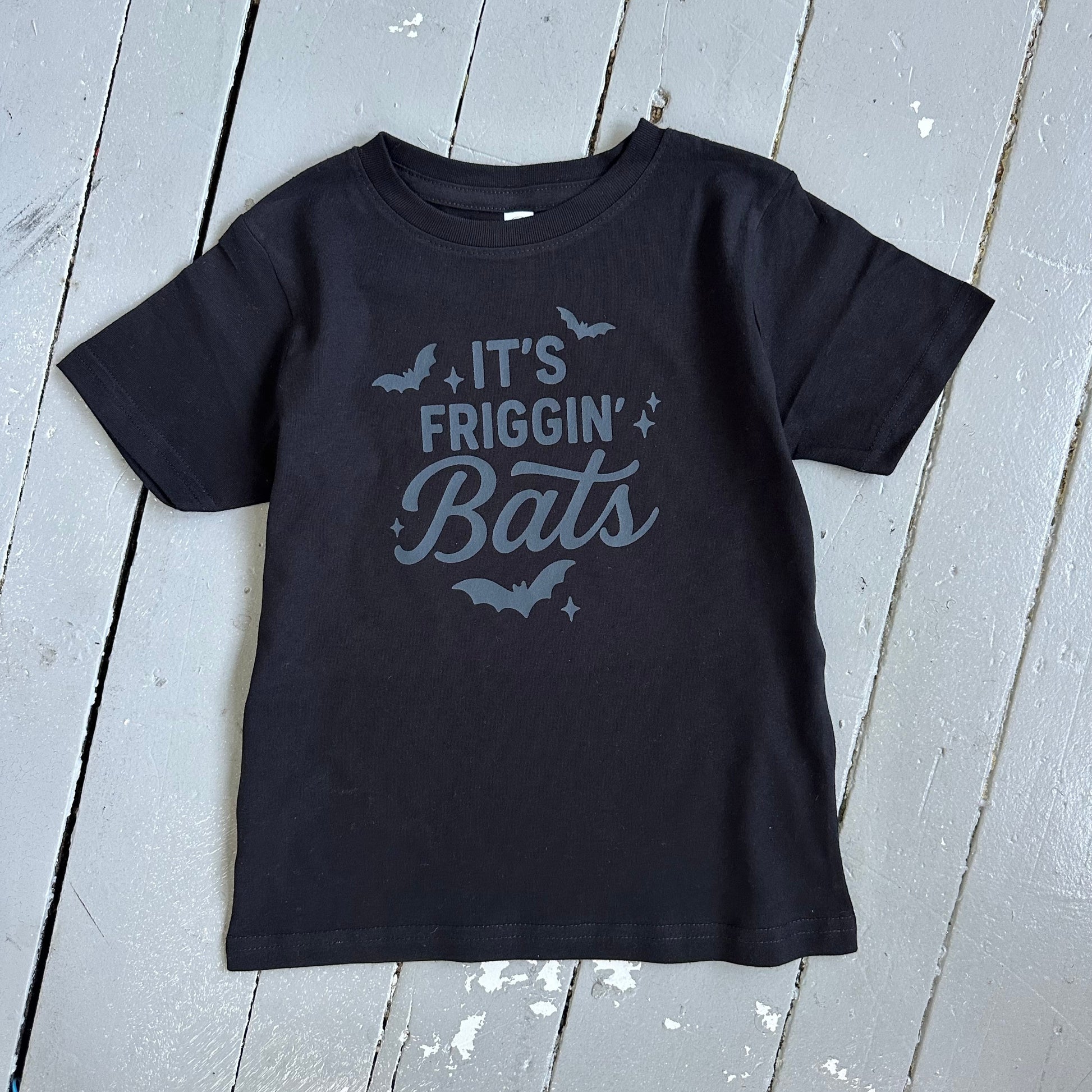 Black t-shirt with 'It's Friggin' Bats' text on a wooden surface
