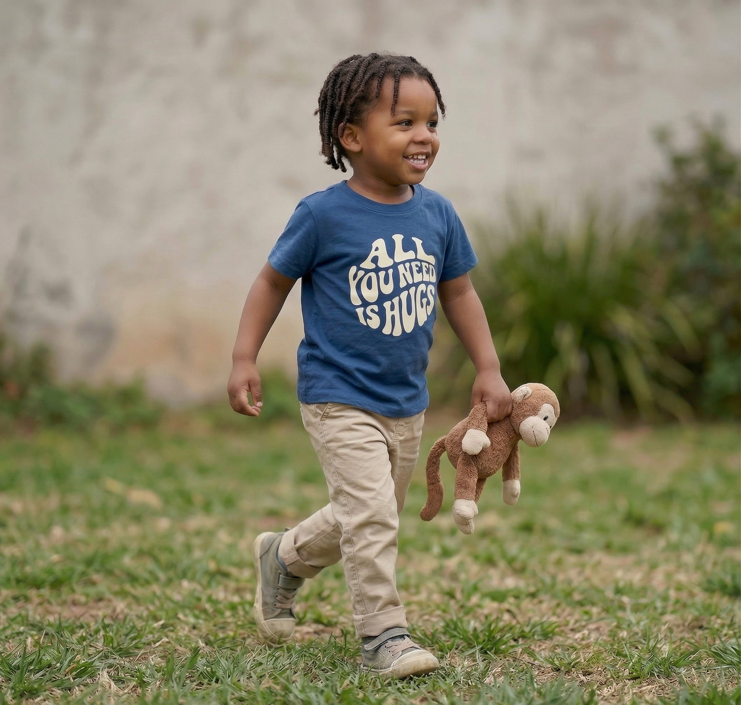Cute toddler wearing The Wishing Elephant All You Need Is Hugs kids graphic T-shirt with hugging heart design.
