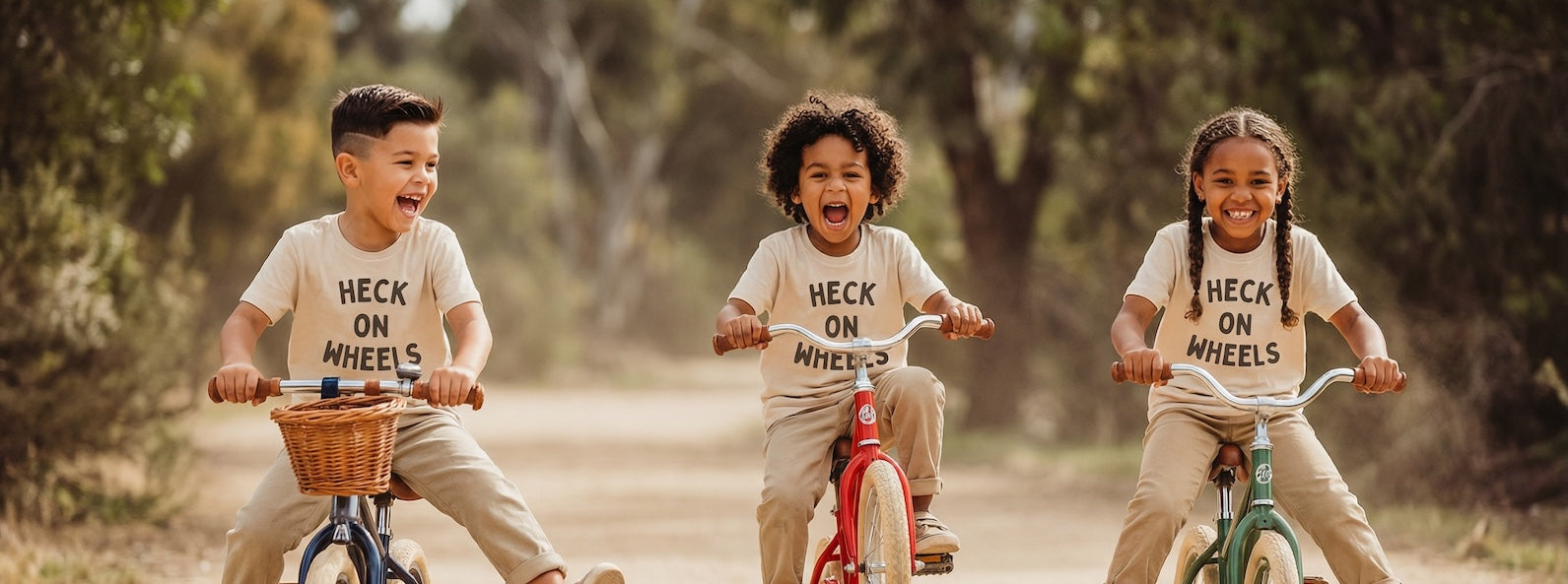 Three children riding bicycles with 'heck on Wheels' shirts in a natural setting.
