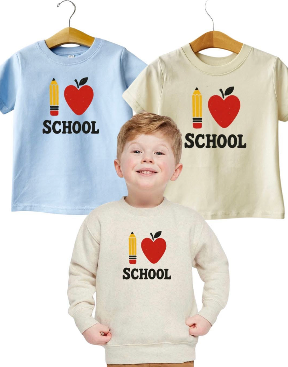 A young child wearing a cream sweatshirt with a school-themed graphic, with two matching short-sleeve t-shirts on hangers behind him. The shirts are light blue and cream, both featuring a yellow pencil, red apple, and the word 'SCHOOL' in black.