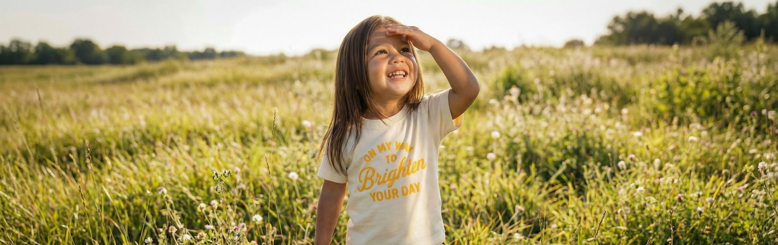 Child standing in a field wearing a t-shirt with text, looking up towards the sky.
