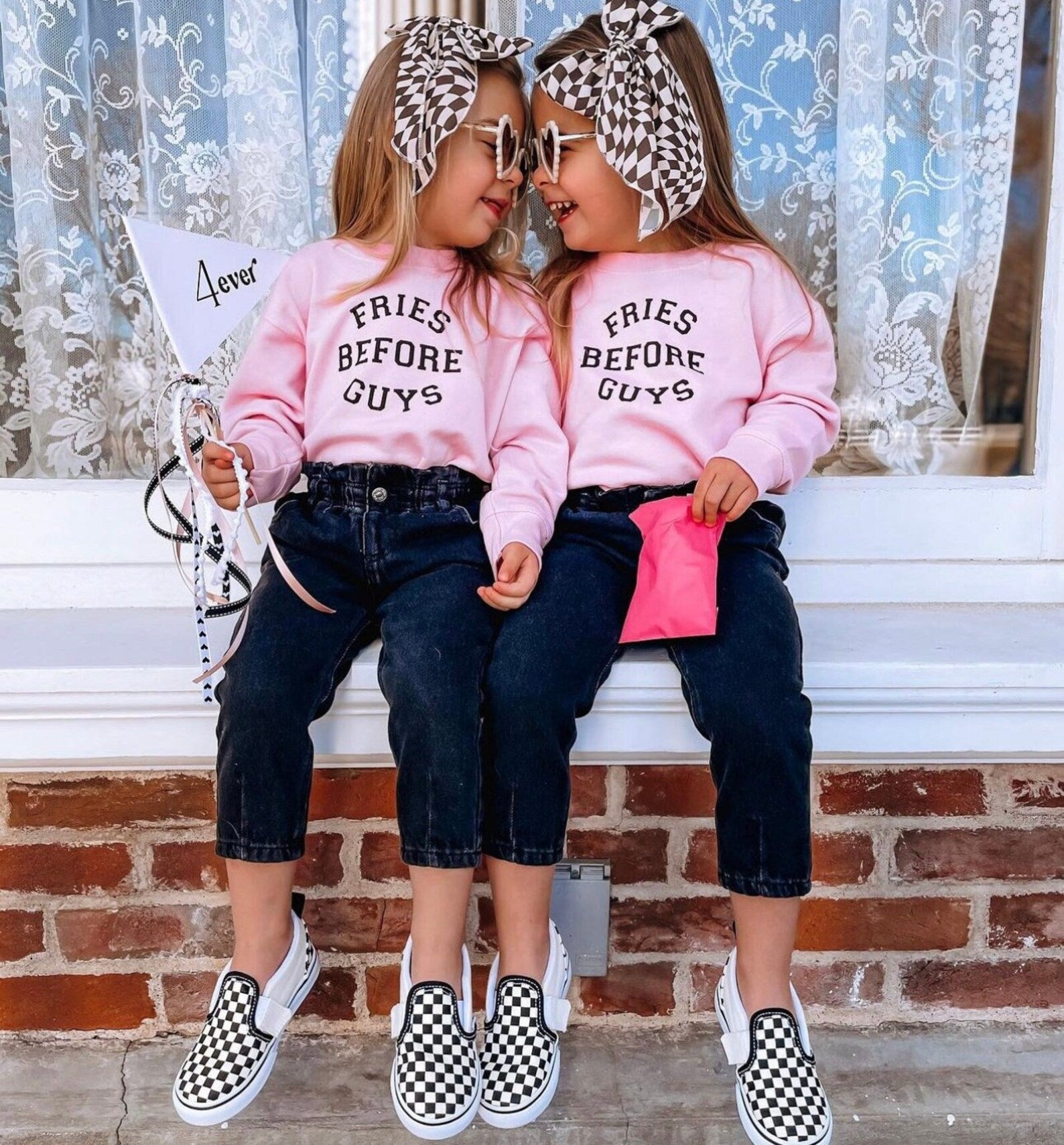 Two girls sitting on brick steps wearing matching Fries Before Guys pullovers