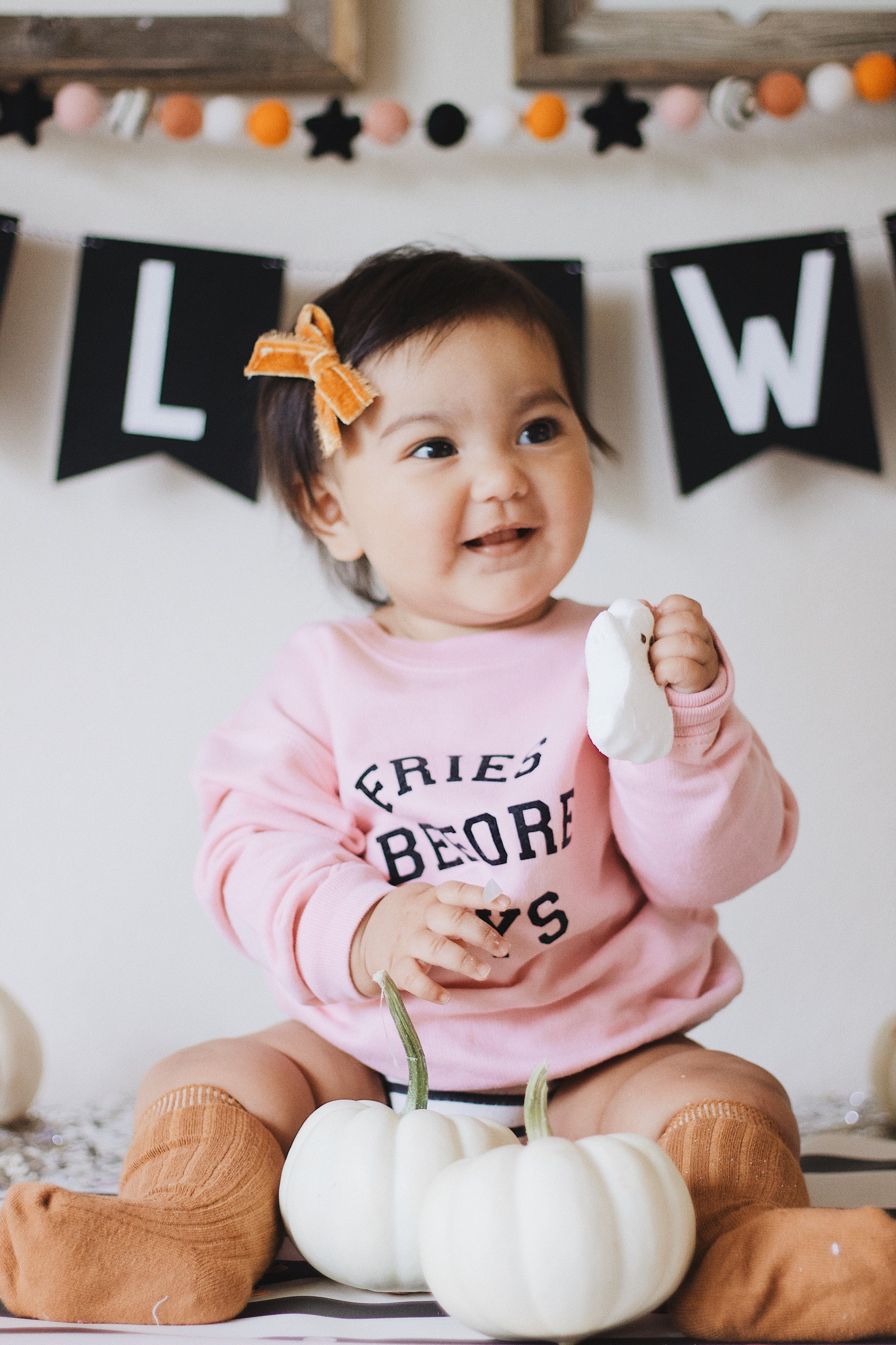 baby playing with pumpkin and a halloween banner behind her she is wearing fries before guys and an orange bow